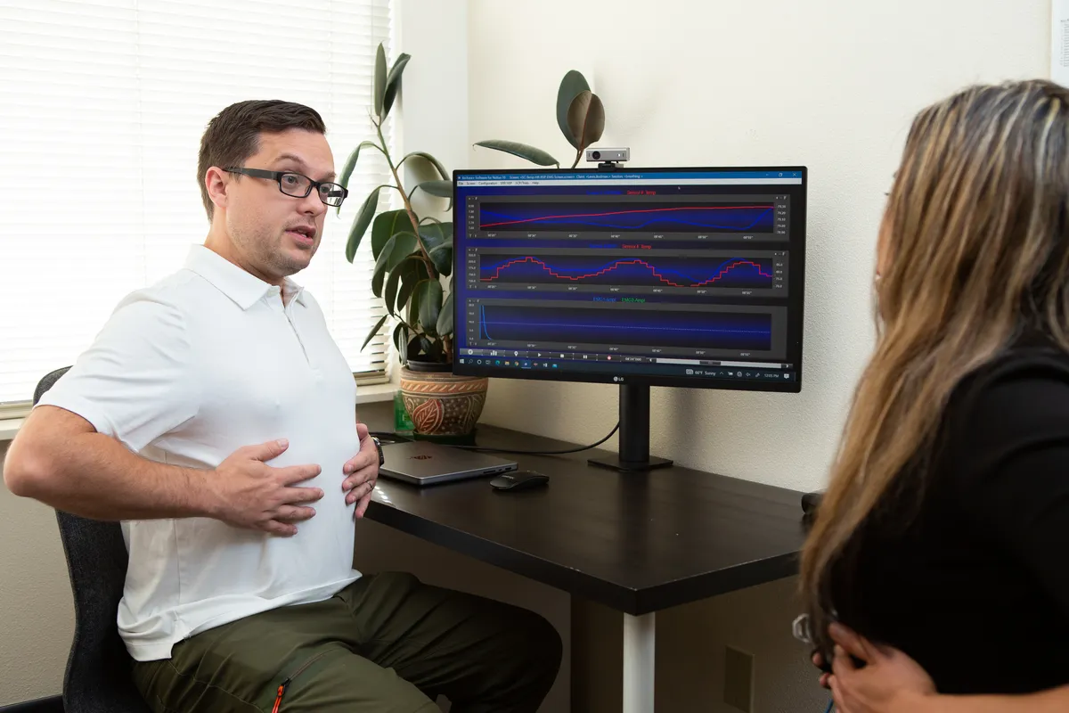 Dr. Andrew Simon demonstrating paced breathing beside a live biofeedback display
