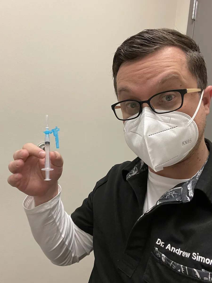 Dr. Andrew Simon in an N95 mask holding a syringe, administering the first COVID-19 vaccine at Rebel Med NW